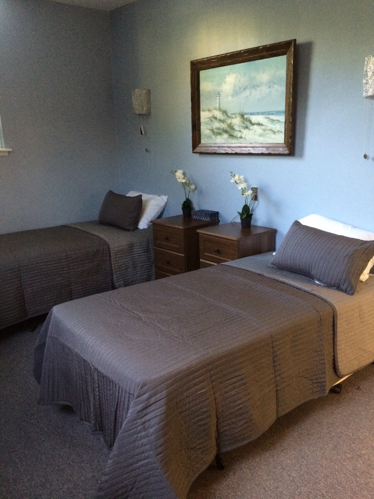 A cozy bedroom with two neatly made twin beds, featuring gray bedding and a wall painting, creating a serene atmosphere.