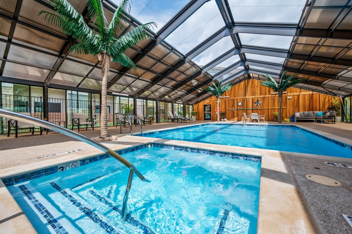 A luxurious indoor swimming pool with a glass roof and palm trees.