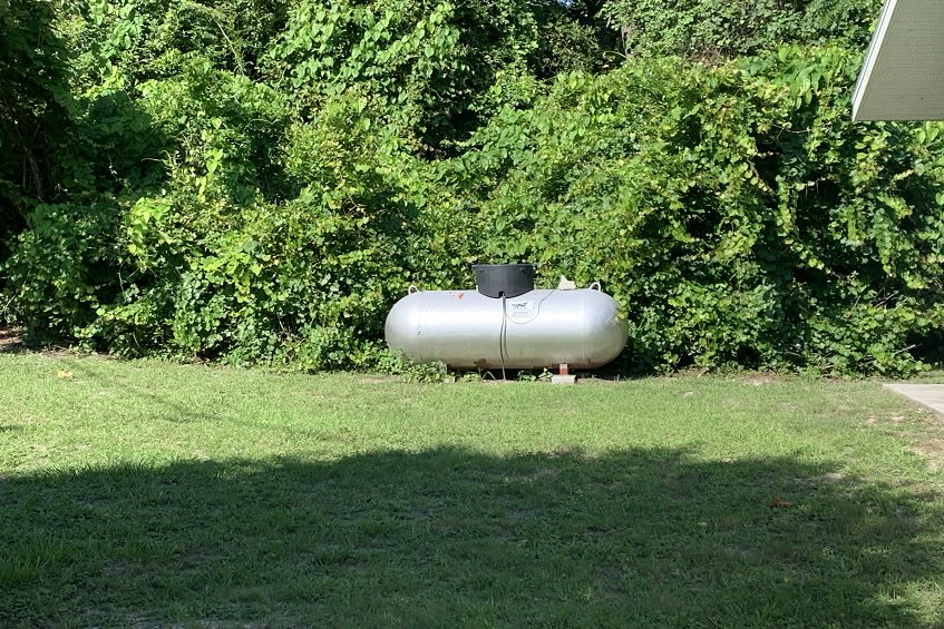 A propane tank placed in a grassy area surrounded by trees and greenery.