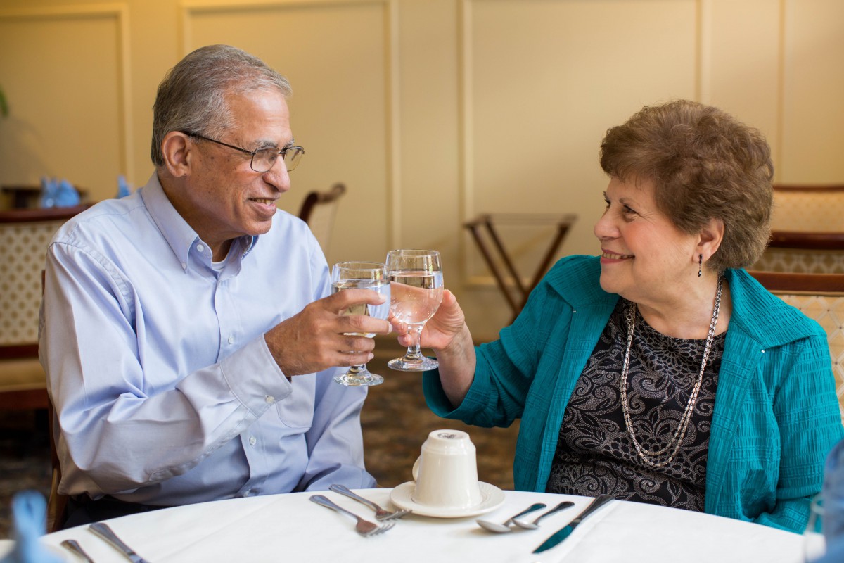 An elderly couple toasting and smiling at a dining table.