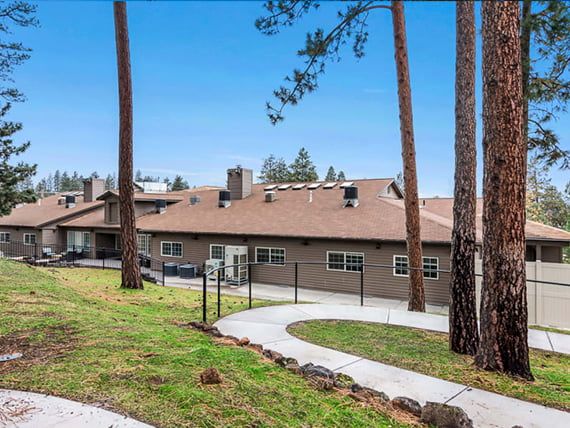 A residential building surrounded by tall trees, with a paved pathway leading to its entrance.