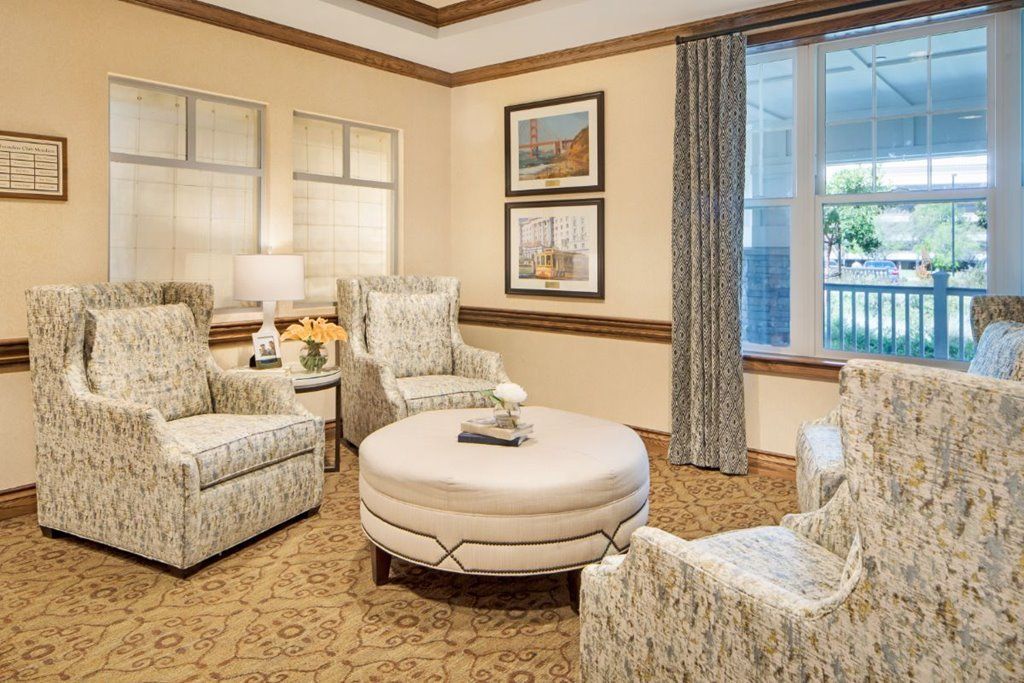 A cozy living room with patterned armchairs, a round coffee table, and framed artwork on the walls.