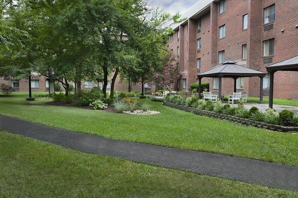 A serene garden with a pathway, surrounded by an apartment building and lush greenery.