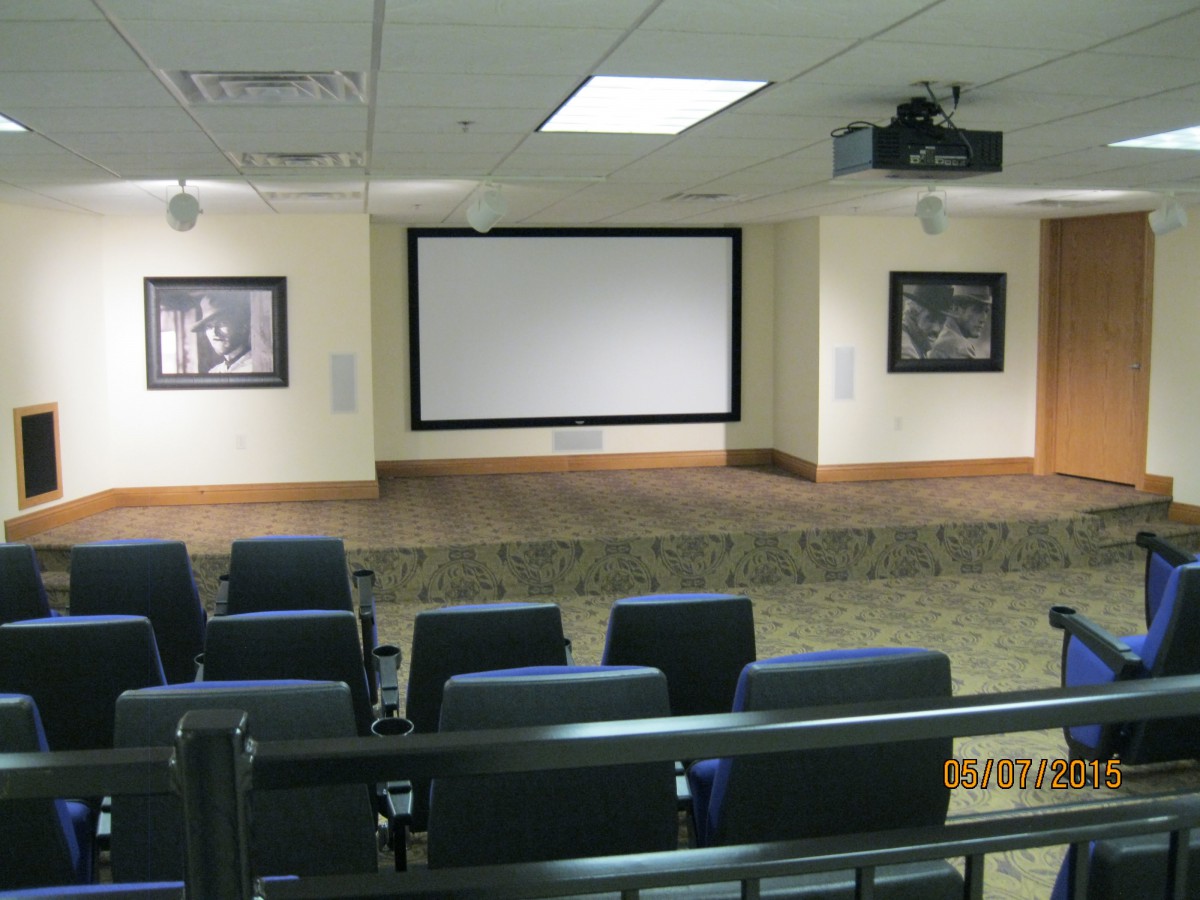 An empty auditorium with a large screen and rows of seats, ready for a presentation.