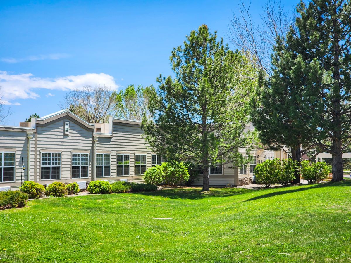 A suburban house with a lush green lawn and surrounding trees under a clear blue sky.