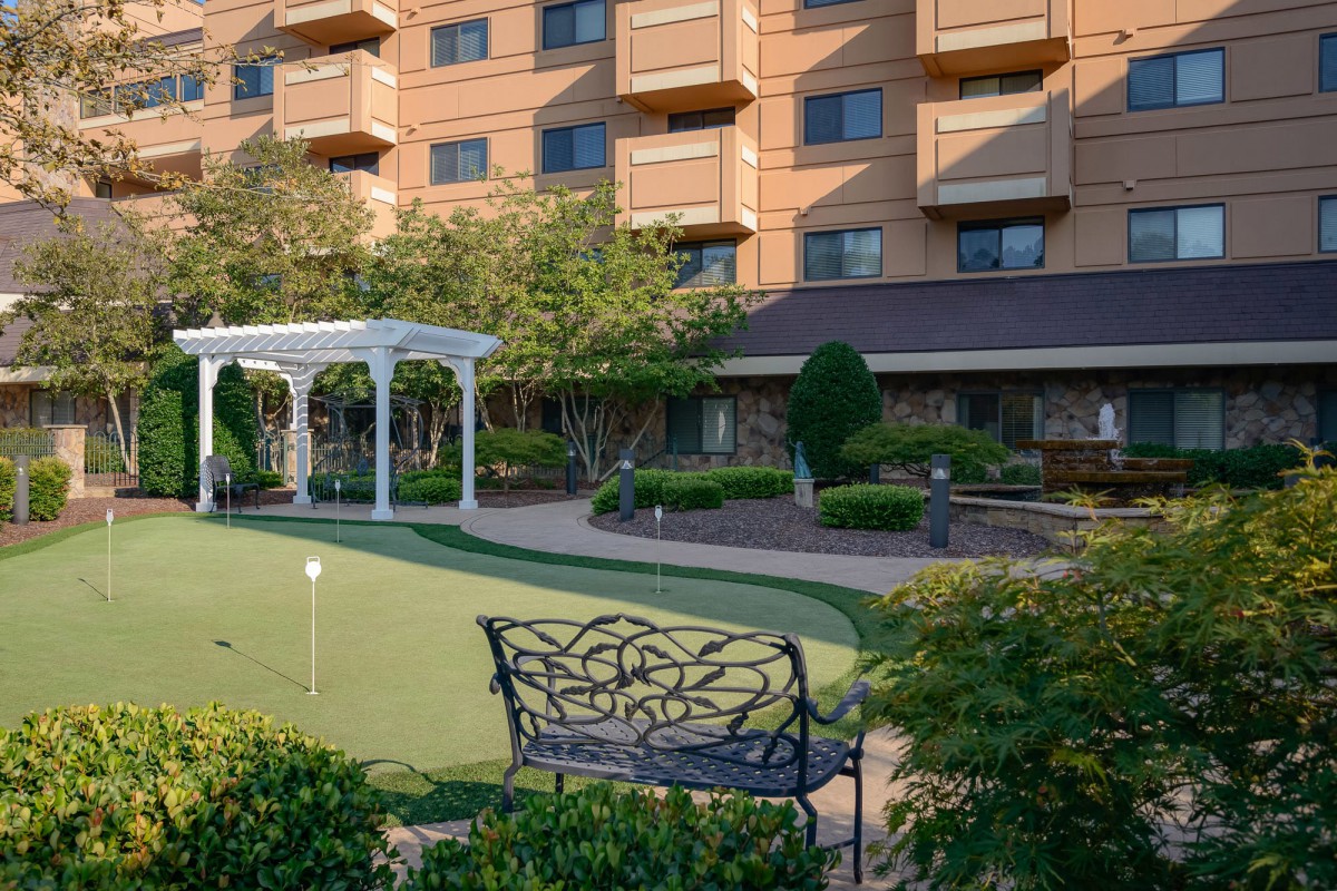 A hotel garden featuring a putting green, with ornate benches and well-maintained landscaping.