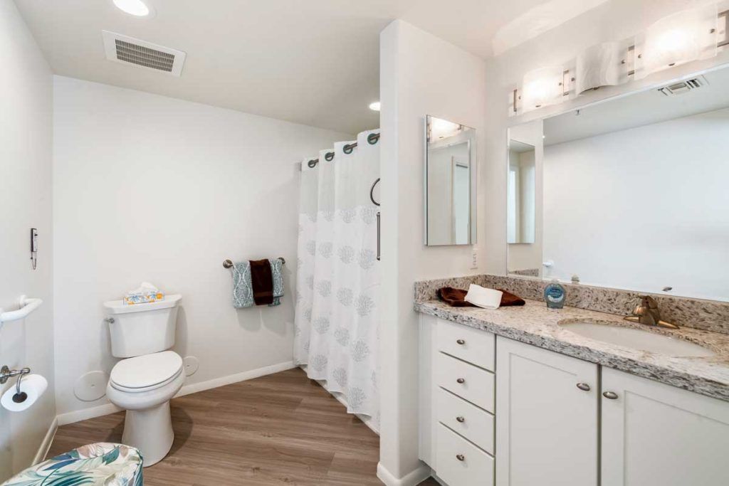 A modern bathroom with white decor and wood flooring, featuring a shower, toilet, sink, and storage cabinets.