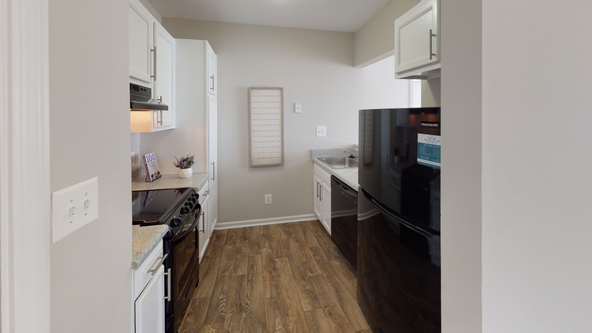 A modern kitchen with white cabinets, hardwood floors, and sleek appliances.