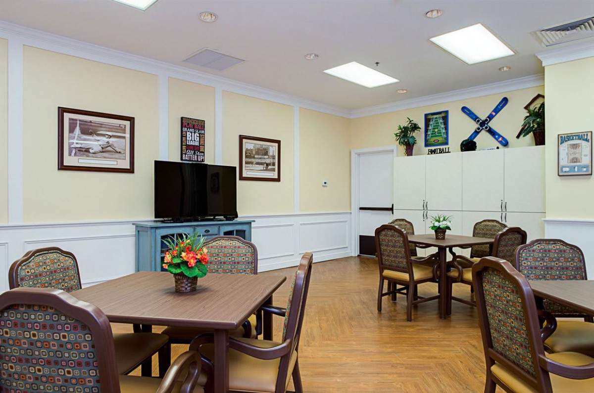 A neatly arranged community room with tables and chairs, decorated with plants and artwork.