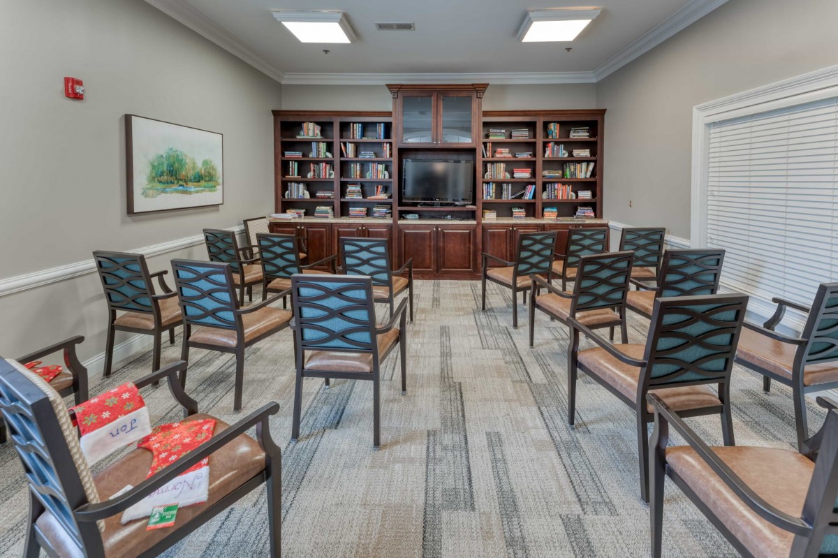 A library-style meeting room with chairs arranged in rows facing a bookshelf with a TV.