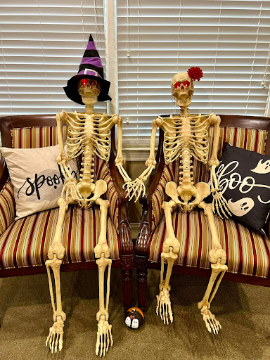 A spooky yet cute Halloween decoration featuring two skeletons holding hands, dressed in festive hats.