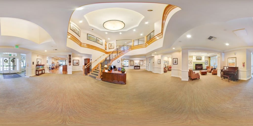 A spacious hotel lobby featuring a grand staircase and a reception desk, elegantly illuminated with modern lighting.