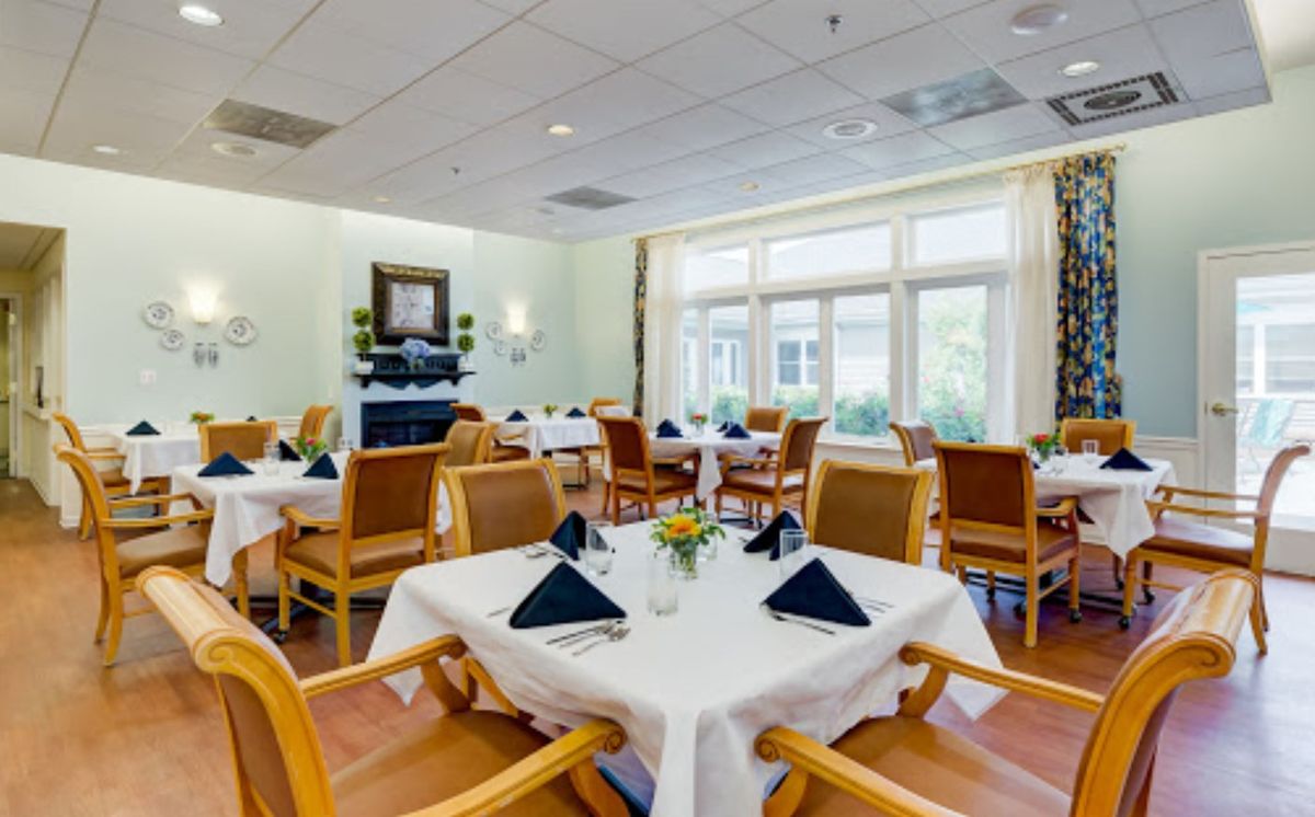 A well-lit dining room with neatly arranged tables and chairs, featuring black napkins on white tablecloths.