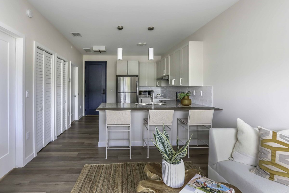A modern, minimalist kitchen in an apartment with a central island and stainless steel appliances.