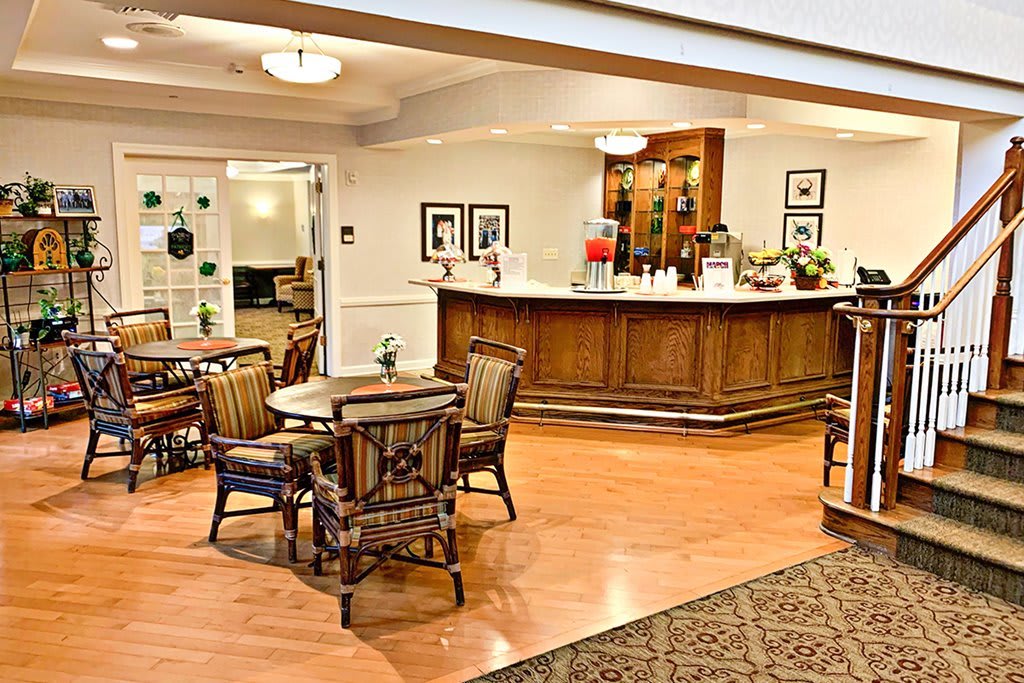 A cozy lounge area with a wooden bar counter and several tables and chairs, featuring warm lighting and decor.