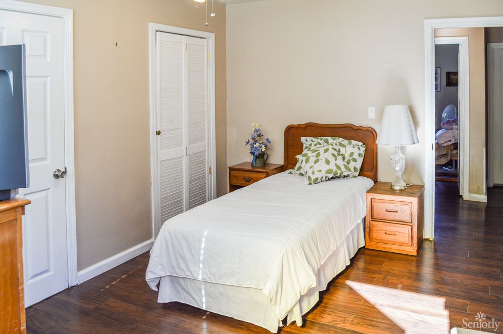 A simple bedroom with a single bed, wooden nightstands, and a lamp on a wooden floor.