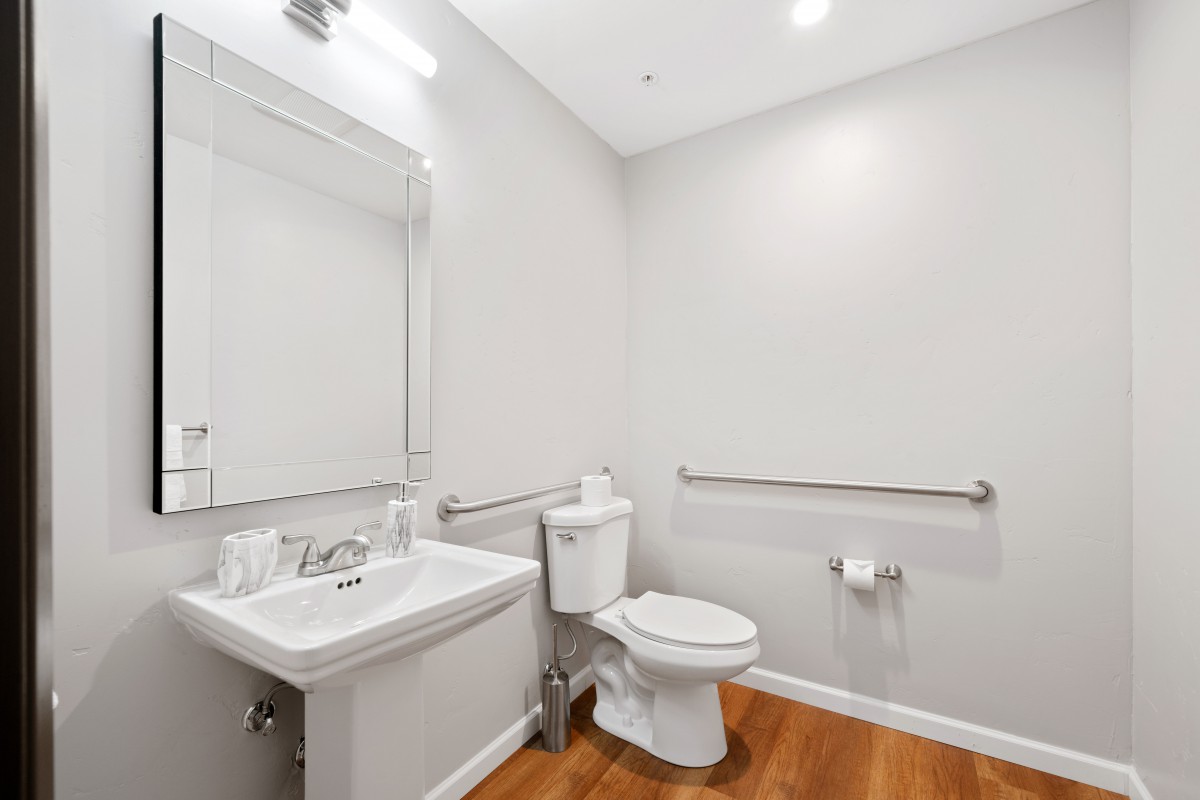 A modern minimalist bathroom with a sink, toilet, and large mirror.