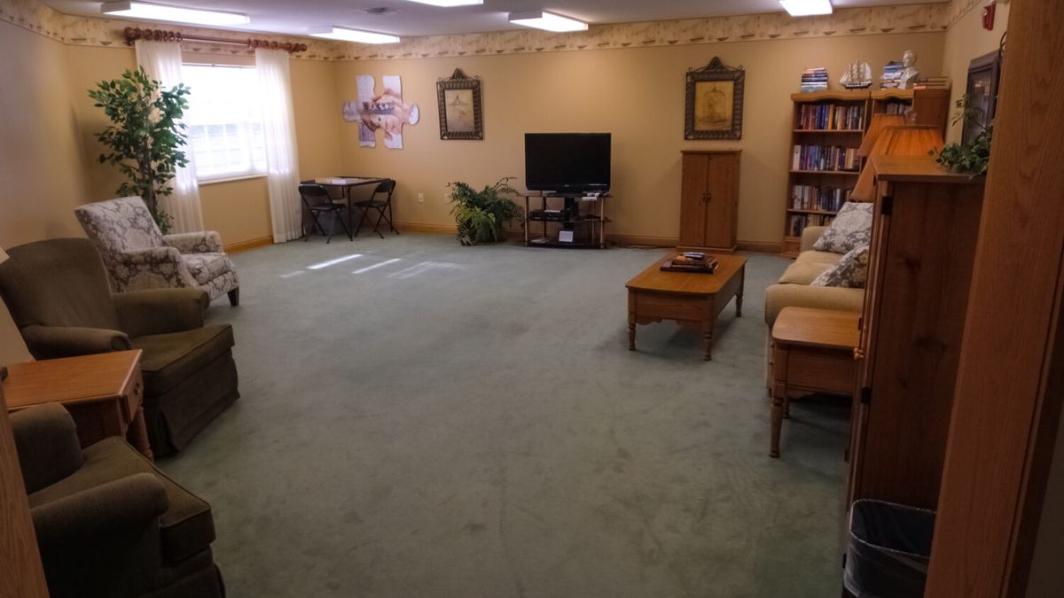 A spacious living room with a sofa, television, and bookshelf on a green carpeted floor.
