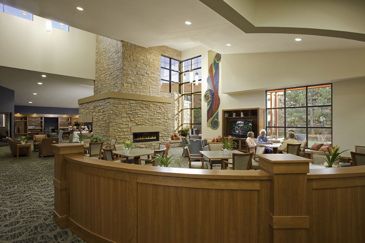 A modern lobby with a central fireplace, comfortable seating, large windows, and wood panel accents.