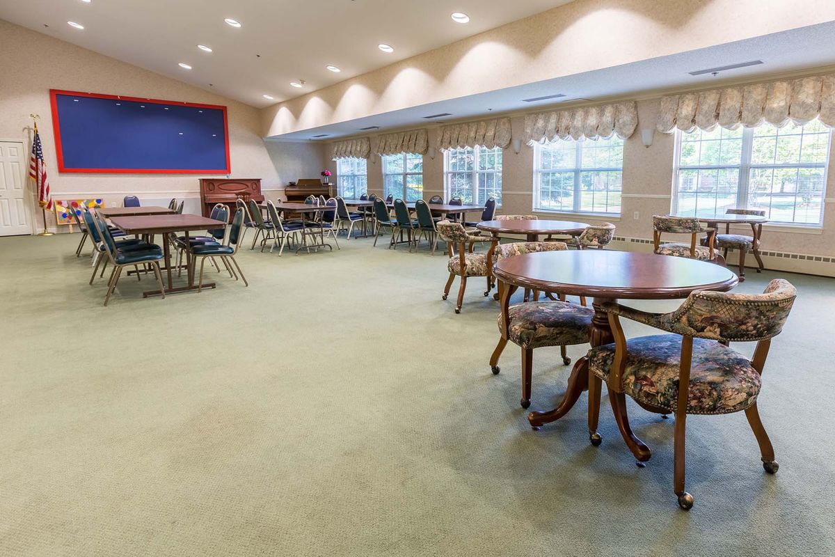 A spacious community center meeting room with tables and chairs arranged on a carpeted floor.