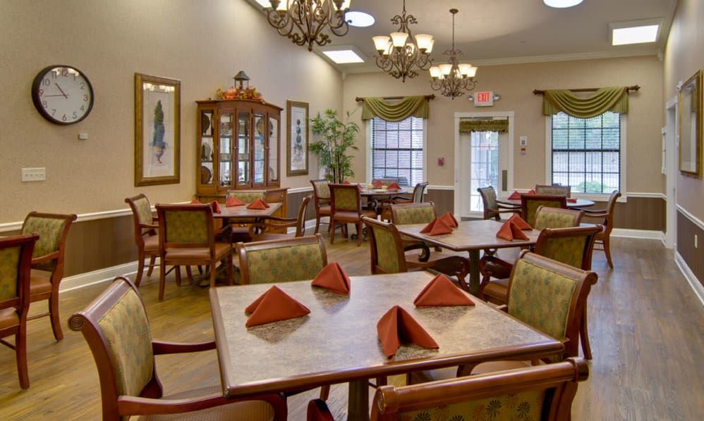 A cozy dining area with neatly arranged tables and chairs, featuring elegant chandeliers and folded napkins.