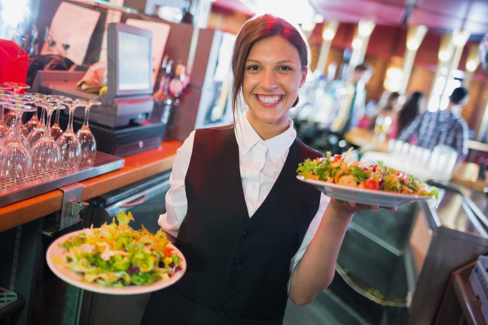 A waitress in a restaurant holding plates of food while smiling.
