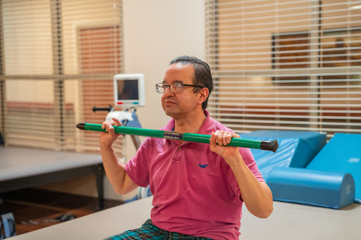 A man performs strength exercises with a green bar during physical therapy.