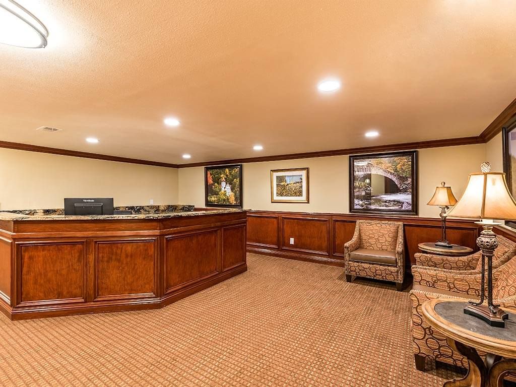A well-furnished office reception area featuring a wooden desk, chairs, and framed artwork on the walls.