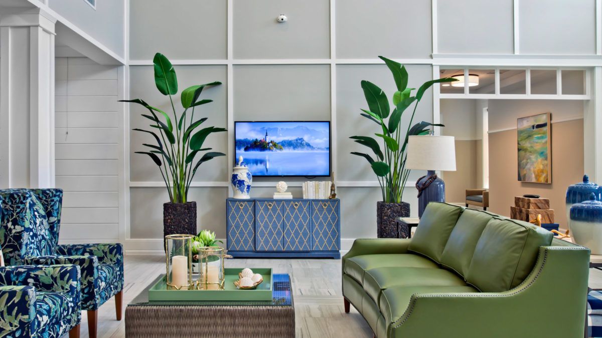 A modern living room with green accents and large indoor plants, featuring a television and stylish decor.