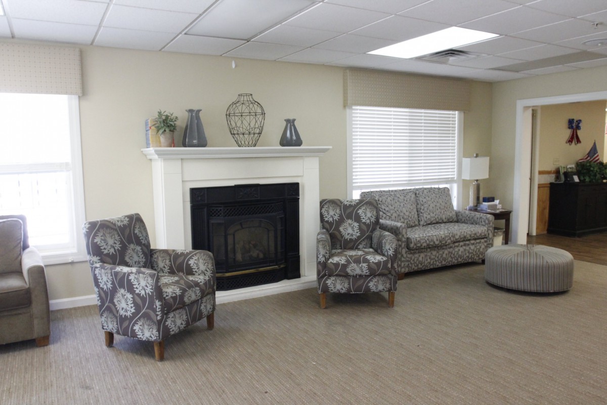 A cozy living room with a fireplace, featuring a sofa and patterned armchairs in neutral tones.