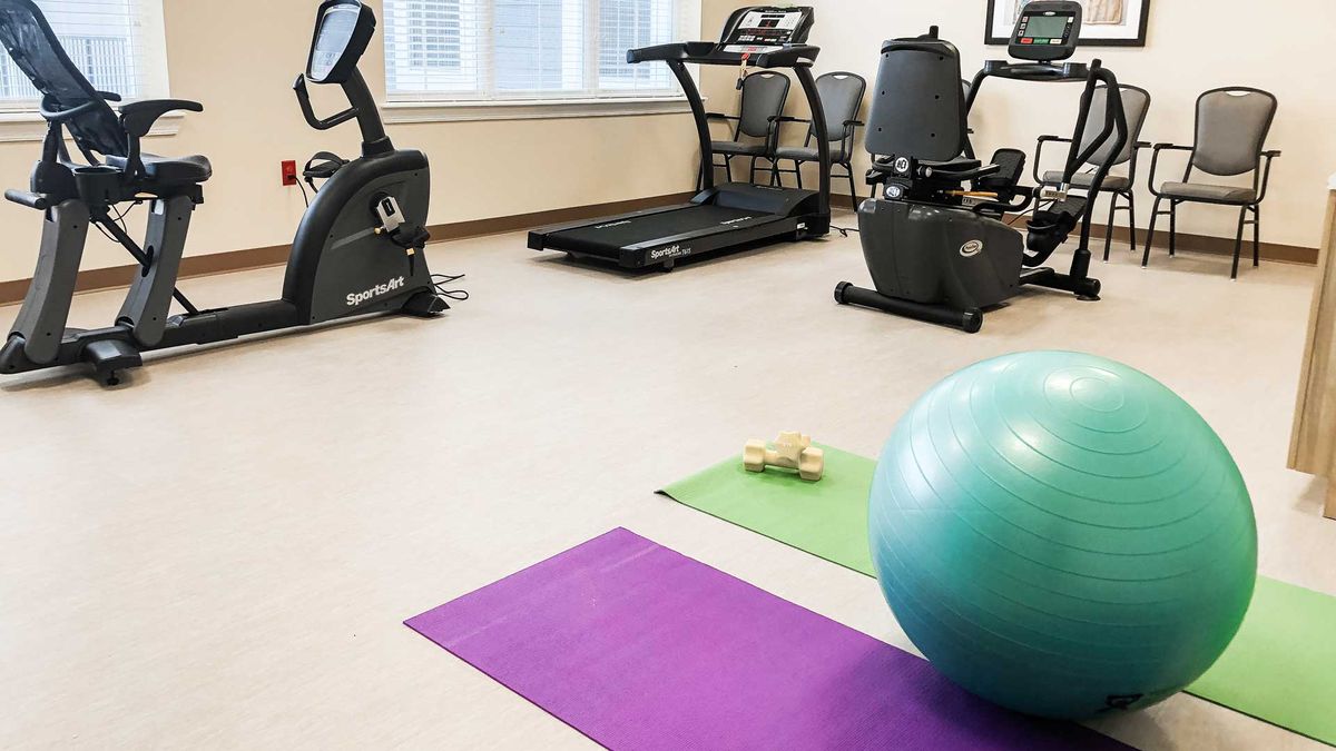 A fitness room equipped with a treadmill, stationary bike, yoga mats, and an exercise ball.