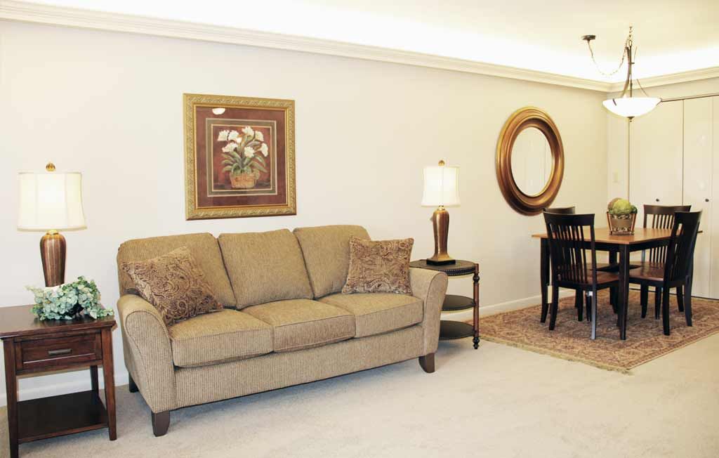 A cozy living room featuring a beige sofa, framed art, and a lamp next to a dining area.