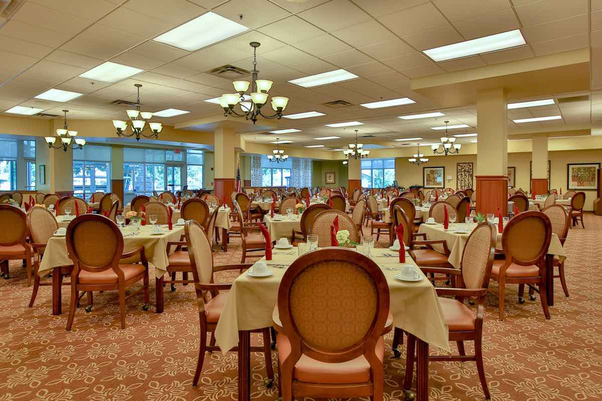 An elegant dining room with neatly arranged tables and chairs, illuminated by chandeliers.
