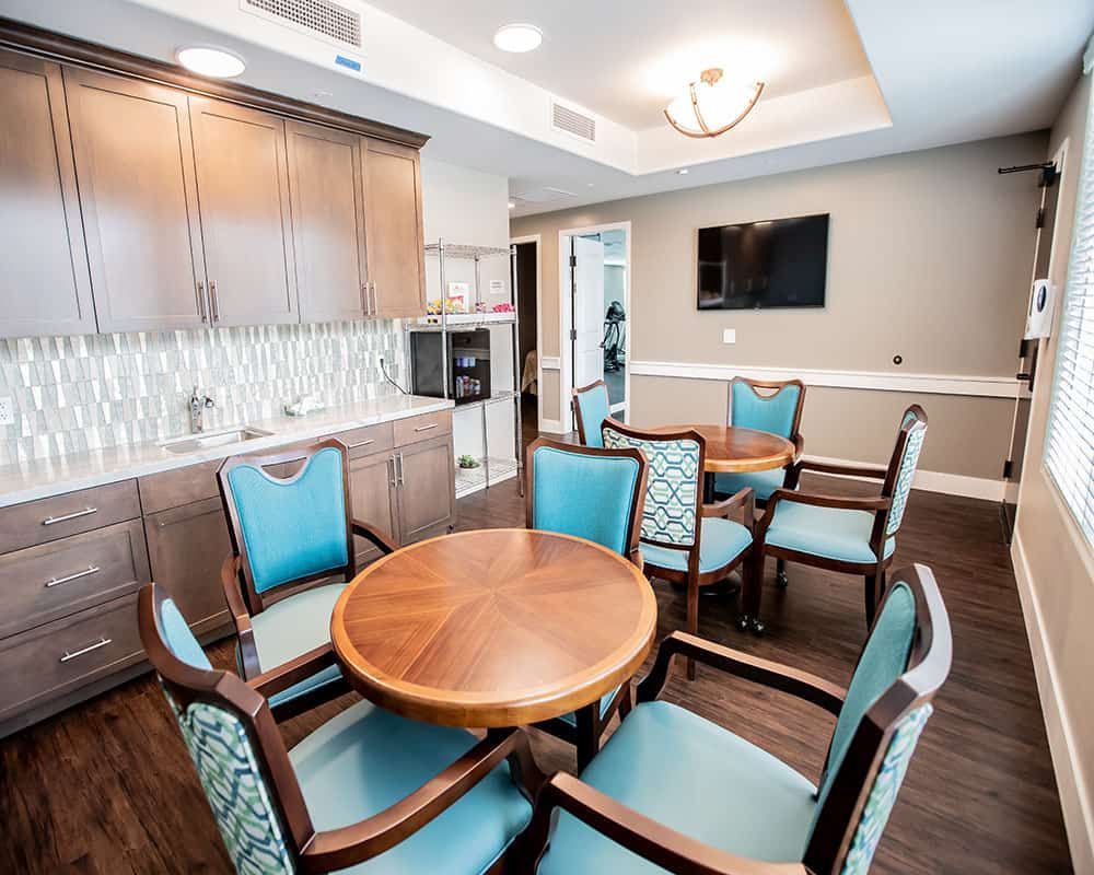 A modern seating area with a round wooden table, cushioned chairs, a wall-mounted TV, and sleek cabinetry.