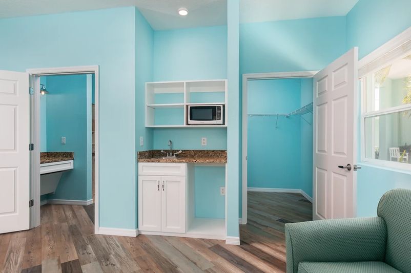 A small kitchenette area with turquoise walls, featuring a microwave and open shelves above a countertop with white cabinets.