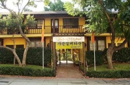 A yellow two-story house with a banner across the entrance, surrounded by trees.