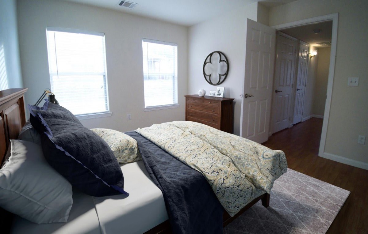 A cozy bedroom featuring a bed with decorative pillows and blankets, a chest of drawers, and a wall clock.