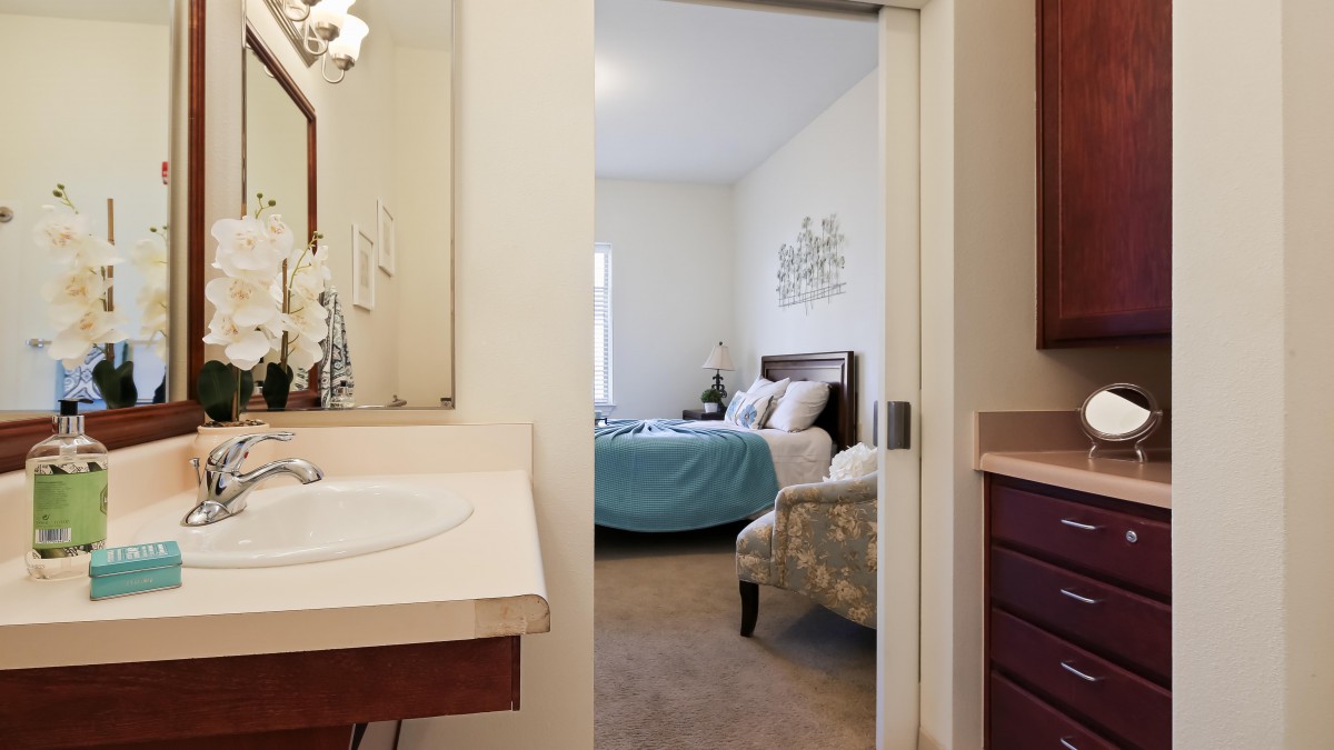 A view from a bathroom into a well-furnished bedroom with a blue bedspread.