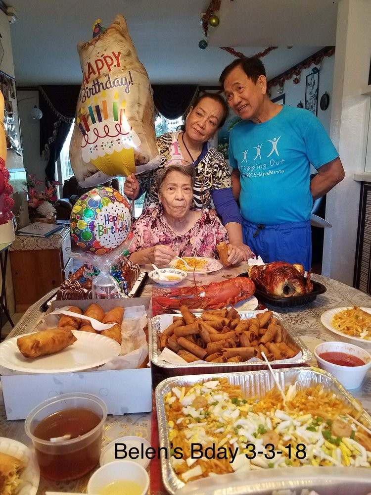A family gathering celebrating a special occasion with a table full of diverse dishes and birthday balloons.
