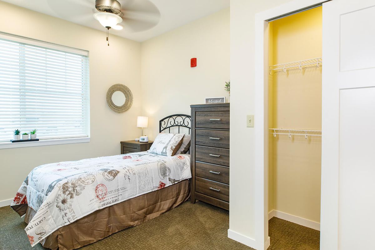 A cozy bedroom with a single bed, dresser, nightstand, and a closet.