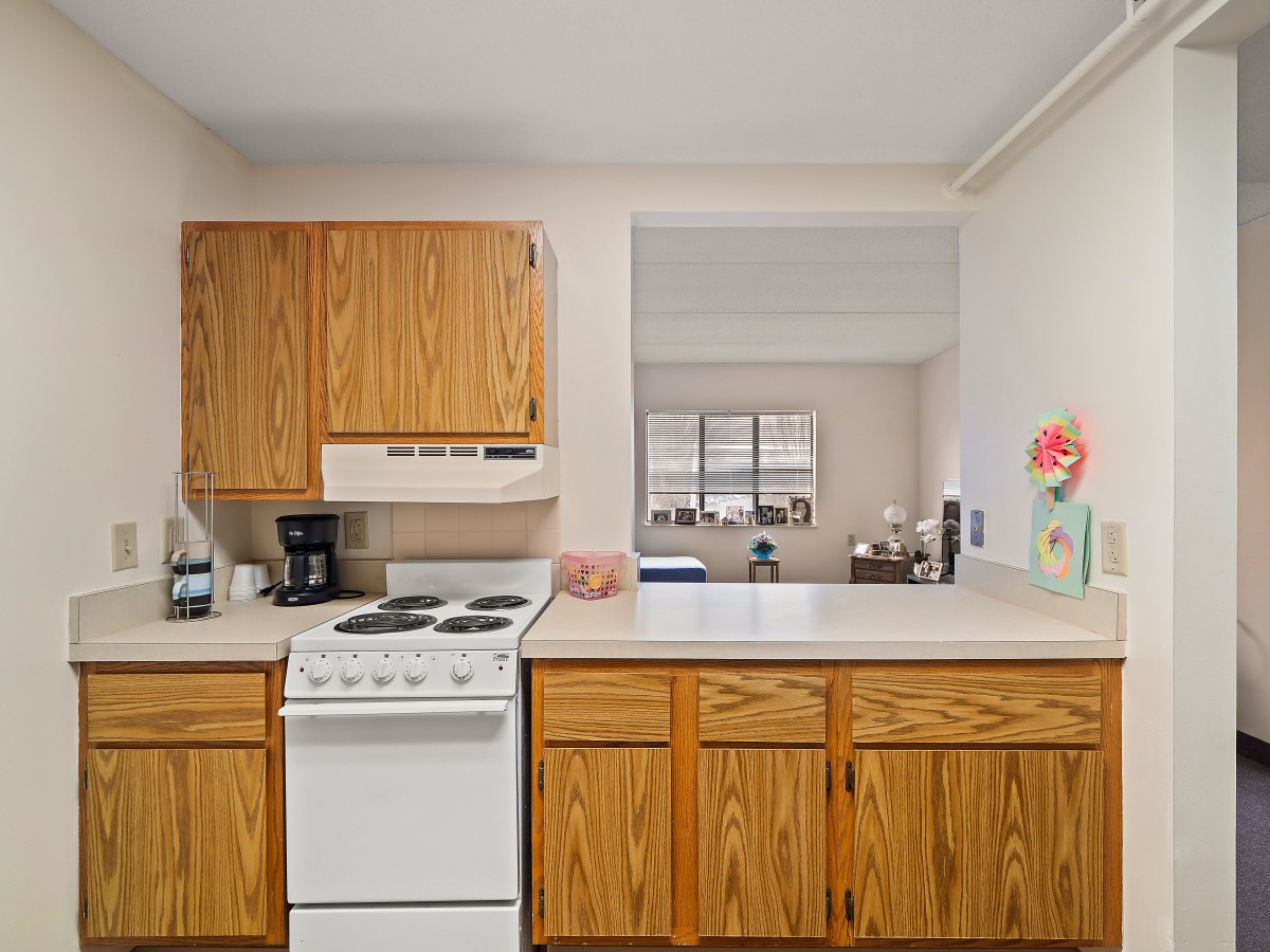 A cozy kitchen with wooden cabinets and a white stove, featuring various appliances on the countertop.
