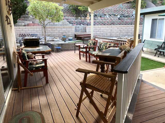 A cozy outdoor patio with wooden decking, featuring various seating arrangements and greenery.