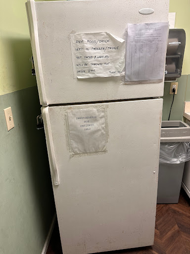 A white refrigerator in a kitchen, with notes attached to its front and a trash can nearby.
