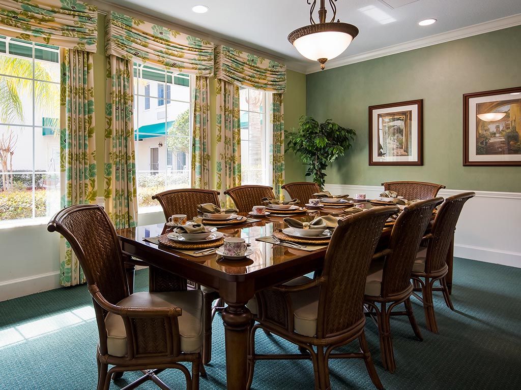 A well-decorated dining room with a large wooden table and chairs, adorned with elegant place settings and surrounded by colorful drapes.