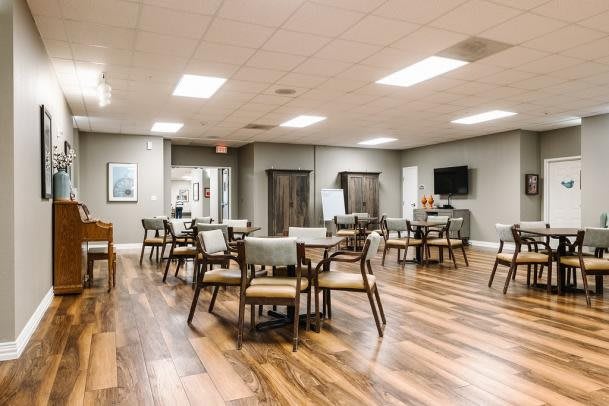 A spacious dining area with wooden flooring, neatly arranged tables and chairs, and ceiling lights.