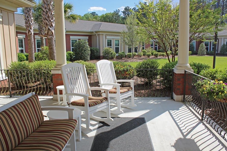 A peaceful porch with white rocking chairs overlooking a well-maintained garden.