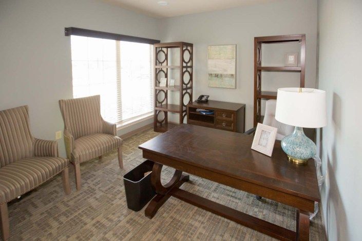 A neat and well-lit home office with a wooden desk, chair, bookshelf, and lamp.