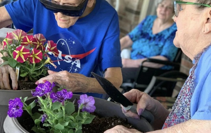 Elderly individuals engaged in gardening activities, with one wearing a NASA shirt and seated by flowers.
