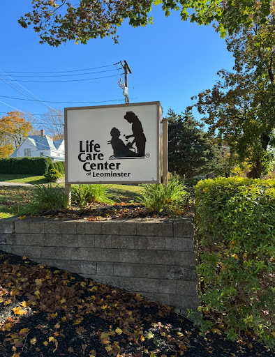 A clear blue sky frames the sign of the Life Care Center, surrounded by greenery.