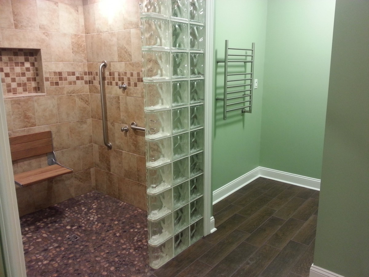 A modern bathroom featuring a walk-in shower with a glass block wall, tiled surfaces, and wood-like flooring.
